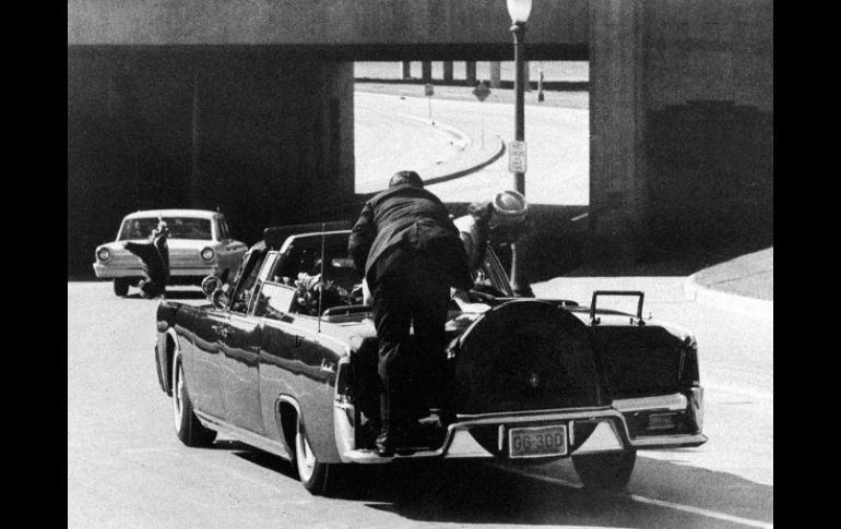 Un agente sube al parachoques de el auto que lleva a John Kennedy herido, mientras su esposa reacciona al atentado. ARCHIVO /