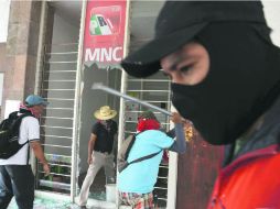 Posibles miembros de la CETEG destrozan la puerta de entrada a la sede estatal del PRI, posteriormente la incendiaron. AP /