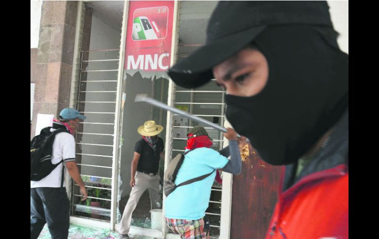 Posibles miembros de la CETEG destrozan la puerta de entrada a la sede estatal del PRI, posteriormente la incendiaron. AP /