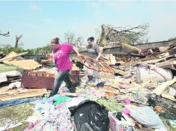 De entre los escombros de una casa, dos mujeres recogen los bienes que se salvaron del tornado. AFP /