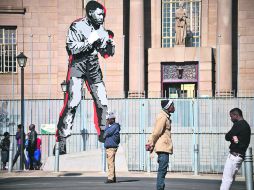 Cautela. Ciudadanos pasan a un lado de la estatua que representa al ex gobernante, en el Centro de Johanesburgo. AFP /