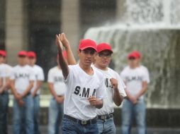 Jóvenes muestran su adiestramiento militar bajo la lluvia en la Plaza Liberación; autoridades, bajo un toldo, los observan.  /