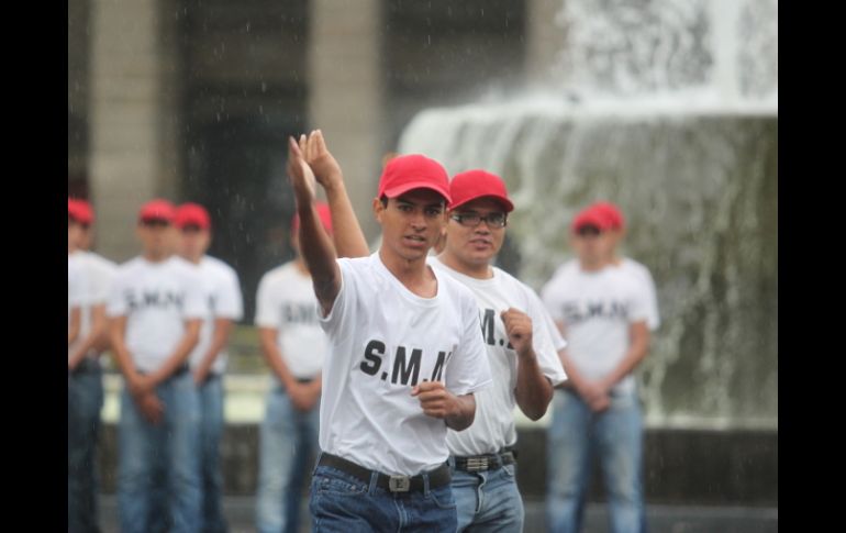 Jóvenes muestran su adiestramiento militar bajo la lluvia en la Plaza Liberación; autoridades, bajo un toldo, los observan.  /