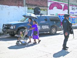 Dos mujeres caminan por las calles de Aguililla, mientras un par de policías federales realizan labores de patrullaje. AFP /