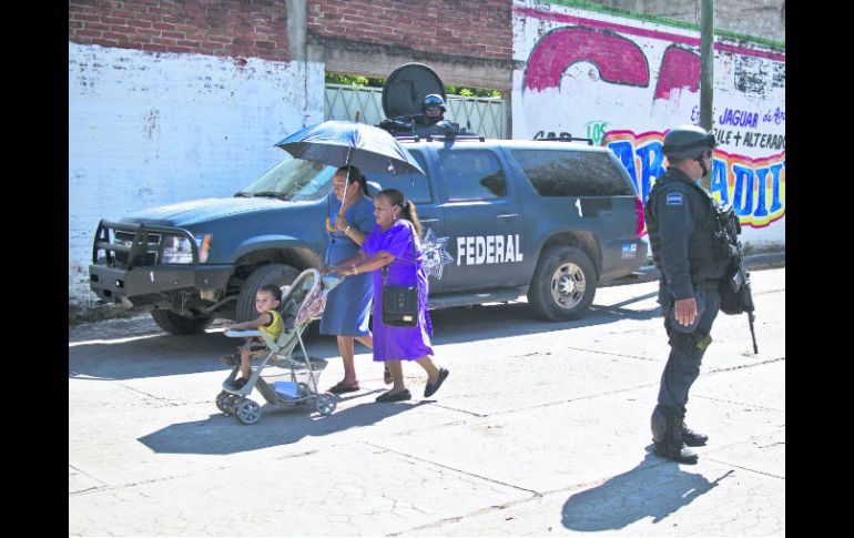 Dos mujeres caminan por las calles de Aguililla, mientras un par de policías federales realizan labores de patrullaje. AFP /