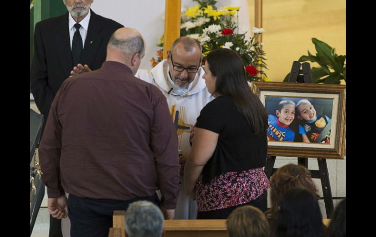 Un sacerdote habla con los padres de los niños fallecidos durante la misa. AP /