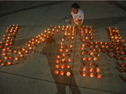 Una mujer enciende veladoras, colocadas en forma de las letras VIH. ARCHIVO /