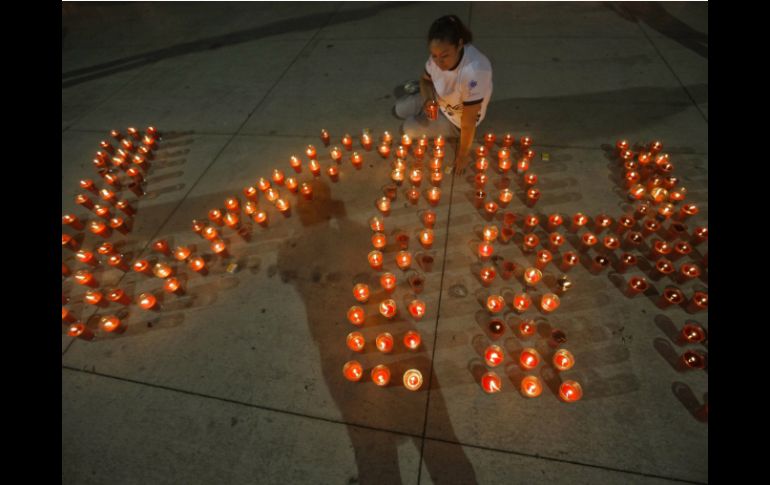 Una mujer enciende veladoras, colocadas en forma de las letras VIH. ARCHIVO /