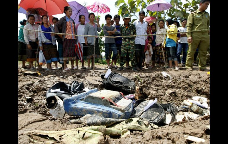 Lugareños observan una zona acotada donde estan varios objetos personales de los pasajeros y restos del fuselaje cerca del río Mekong. EFE /