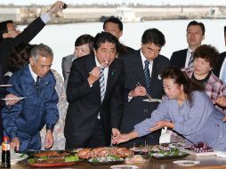 El ministro Abe (c) comió pescado y pulpo capturado cerca del puerto para dejar claro que son productos seguros. AFP /