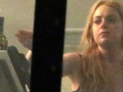 Lohan aparece a punto de tomar una botella de vino, aunque no hay evidencia de que bebiera. ESPECIAL /