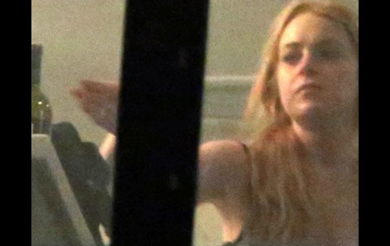 Lohan aparece a punto de tomar una botella de vino, aunque no hay evidencia de que bebiera. ESPECIAL /