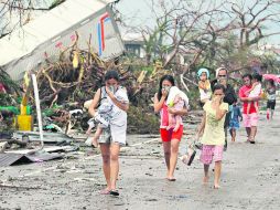 E. Residentes de la ciudad de Tacloban que sobrevivieron a la tragedia pasan frente a escombros cargando a sus hijos. AP /