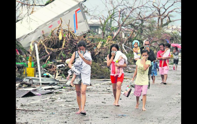 E. Residentes de la ciudad de Tacloban que sobrevivieron a la tragedia pasan frente a escombros cargando a sus hijos. AP /