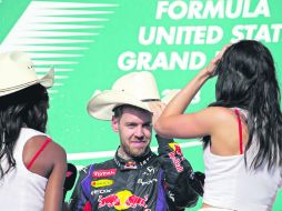 Sebastian Vettel se coloca uno de los tradicionales sombreros texanos ante la mirada de dos edecanes, durante la ceremonia de premiació AP /