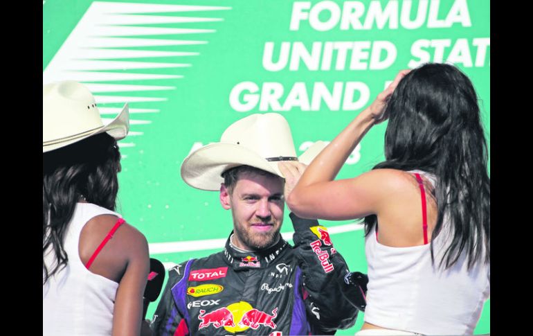 Sebastian Vettel se coloca uno de los tradicionales sombreros texanos ante la mirada de dos edecanes, durante la ceremonia de premiació AP /