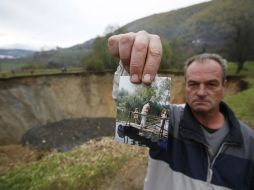 Un hombre sostiene una fotografía de cómo era la laguna, a sus espaldas se puede apreciar el socavón vacío. AP /