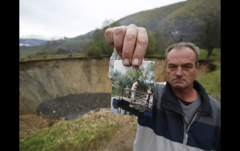 Un hombre sostiene una fotografía de cómo era la laguna, a sus espaldas se puede apreciar el socavón vacío. AP /