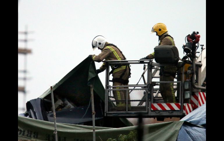 Bomberos observan la parte expuesta de la cola del helicóptero sobre el pub Clutha. AP /