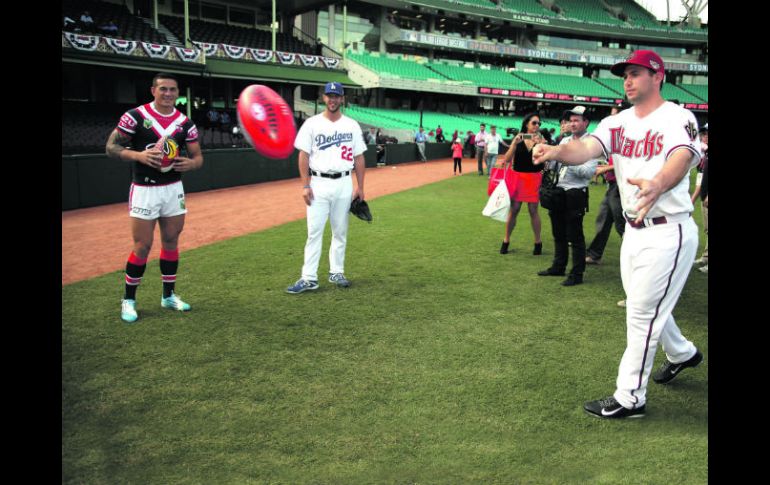 Paul Goldschmidt lanza un ovoide de rugby, mientras el abridor de los Dodgers, Clayton Kershaw (centro), lo observa.  /