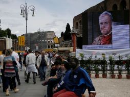 Turistas en Roma pasan junto a una pantalla gigante en que se realizan pruebas, sobre la avenida que lleva al Coliseo. AP /