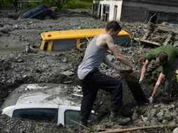 Ciudadanos de Bosnia buscan excavar su automóvil enterrado entre el lodo producido por las inundaciones. AP /