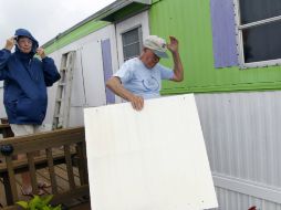 Dos ciudadanos resguardan su vivienda de los fuertes vientos originados por 'Arthur'. AP /