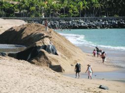 Paseantes en Barra de Navidad caminan cerca de los montículos de arena que serán distribuidos para rehabiltar la playa. ESPECIAL /