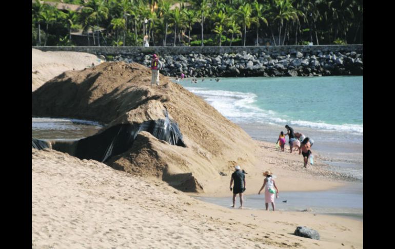 Paseantes en Barra de Navidad caminan cerca de los montículos de arena que serán distribuidos para rehabiltar la playa. ESPECIAL /