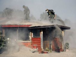 Policías chilenos quitan la ceniza que cayó en el techo de una casa en La Ensenada. AFP /  Policías chilenos quitan la ceniza que cayó