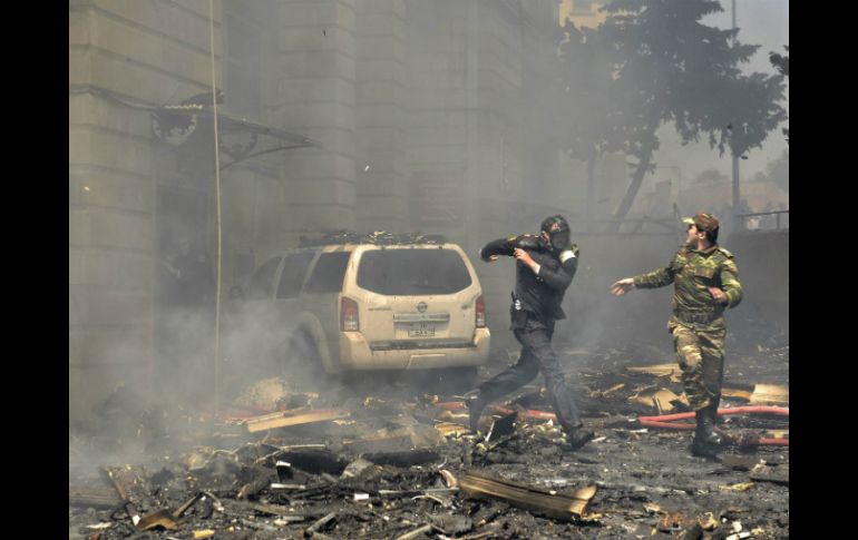 Dos policías corren escapando de los escombros que caen del edificio incendiado en Bakú. EFE / O. Azim