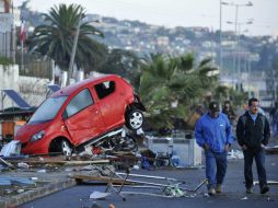 Dos hombres caminan frente a un vehículo arrastrado por el tsunami posterior al terremoto 8.4 que anoche sufrió Chile. EFE / A. Pizarr