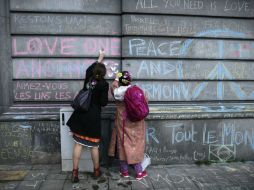 Luto urbano. Un par de mujeres pegan ofrendas en un muro de la capital belga. AFP / K. Tribouillard