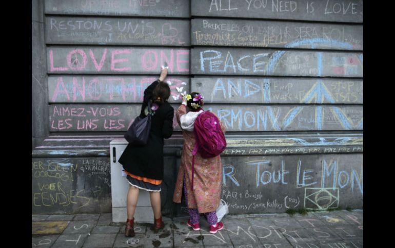 Luto urbano. Un par de mujeres pegan ofrendas en un muro de la capital belga. AFP / K. Tribouillard