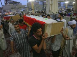 Participantes de un funeral multitudinario cargan ataúdes con los restos de sus seres queridos que ayer fallecieron en la explosión. AP / A. Khalil