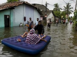 Un sujeto transporta a varias niñas con la ayuda de un colchón inflable hacia un lugar seguro en medio del agua. AP / E. Jayawardena