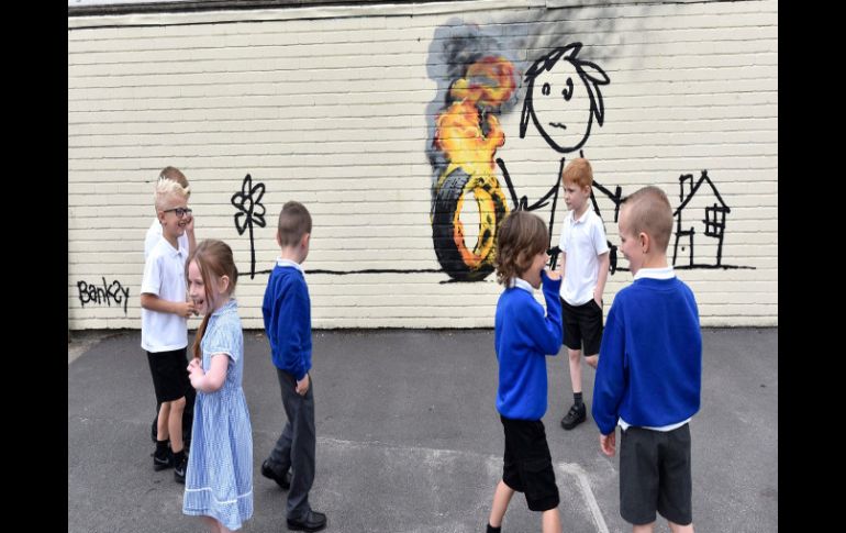 Varios pequeños observan la pintura, en la que se aprecia a una niña jugando con una llanta en llamas. EFE / N. Munns