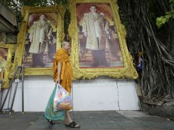 Un monje budista pasa cerca de varios retratos del rey Bhumibol, que son adquiridos por familias con motivo de las fiestas. AP / S. Lalit