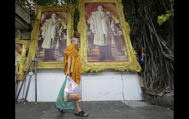 Un monje budista pasa cerca de varios retratos del rey Bhumibol, que son adquiridos por familias con motivo de las fiestas. AP / S. Lalit