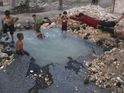 Niños juegan en un enorme agujero lleno de agua, el cual fue causado por la explosión de un proyectil. AP /