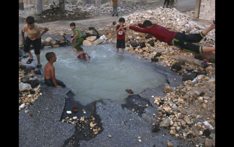 Niños juegan en un enorme agujero lleno de agua, el cual fue causado por la explosión de un proyectil. AP /