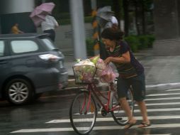 Una mujer trata de caminar con su bicicleta ante los fuertes vientos. AFP / S. Yeh