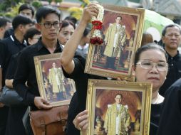 Personas esperaban su turno en las largas filas sosteniendo retratos del fallecido rey. EFE / N. Sangnak