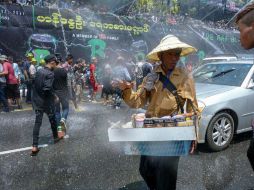 Un sujeto protegido con un sombrero e impermeable intenta vender dulces y cigarros en medio de una batalla de agua. AFP / R. Schmidt