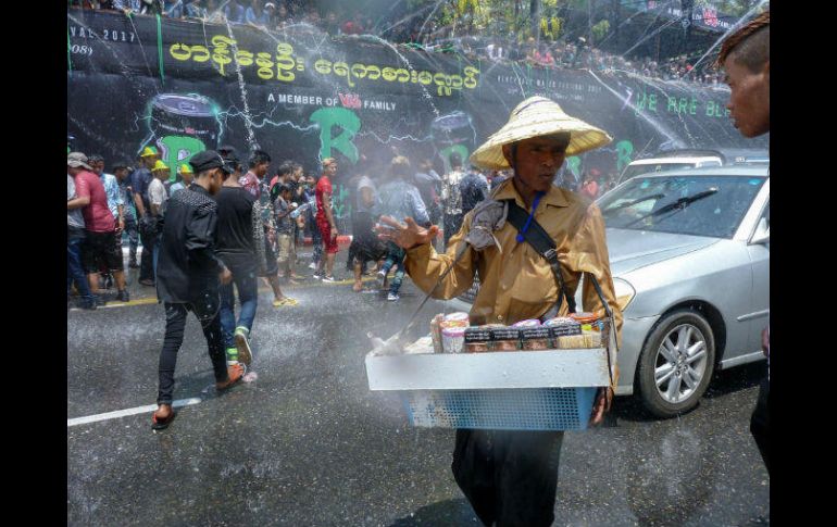 Un sujeto protegido con un sombrero e impermeable intenta vender dulces y cigarros en medio de una batalla de agua. AFP / R. Schmidt