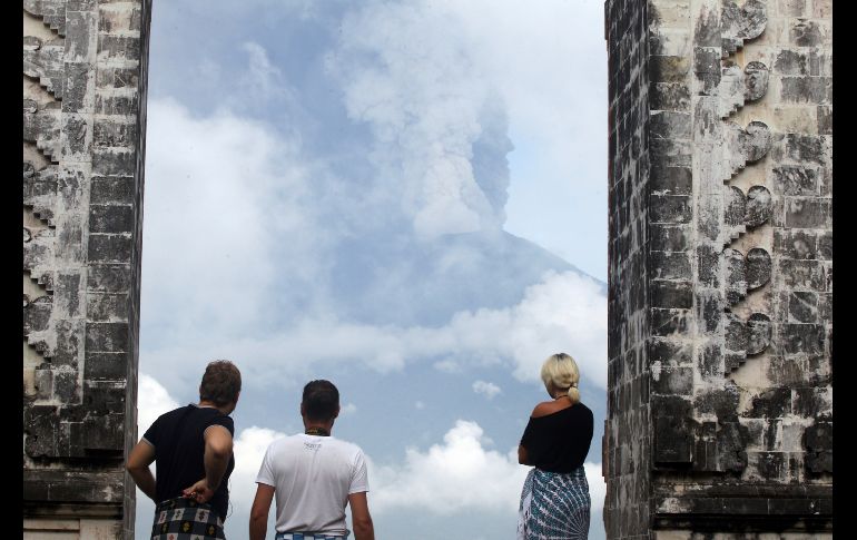 Turistas observan el volcán Agung en erupción mientras visitan un templo en Karangasem, Indonesia. Las autoridades elevaron hoy al máximo la alerta, ordenaron evacuar a unas 100 mil personas y cerraron el aeropuerto. AP/F. Lisnawati