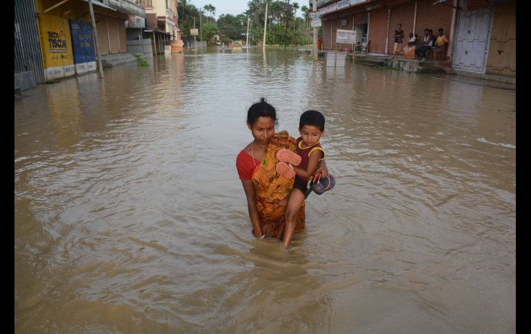 Una mujer carga a un niño en una calle inundada tras fuertes lluvias en Baldakhall, India. AFP/A. Dey