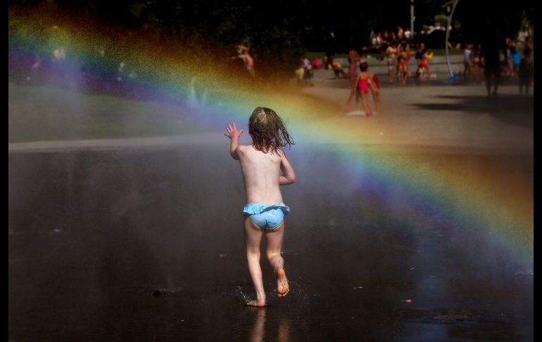 Una niña corre hacia un arcoíris en la fuente de un parque en Madrid, España. AP/A. Comas