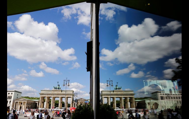 Personas pasan por la puerta de Brandenburgo, que se refleja en la ventana de una tienda en Berlín, Alemania. AP/M. Karout