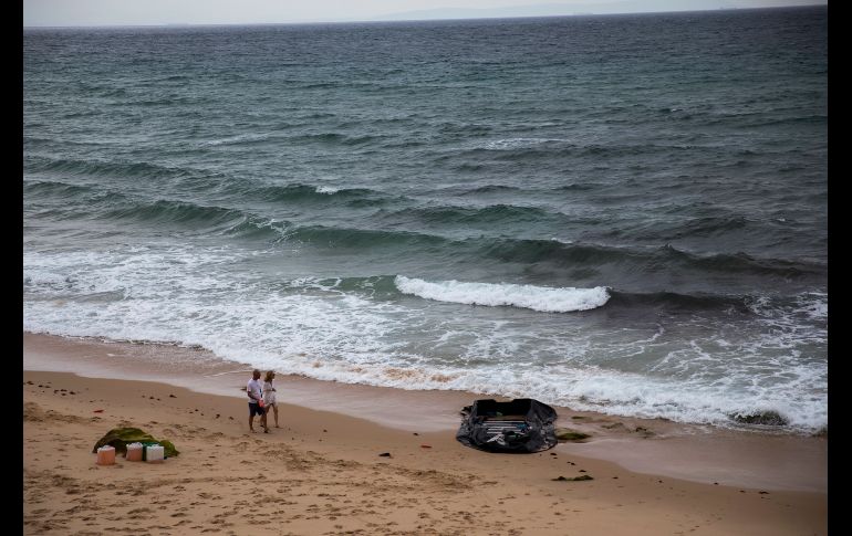 Turistas pasan junto a un bote inflable usado por migrantes marroquíes cerca de Tarifa, España. AP/E. Morenatti